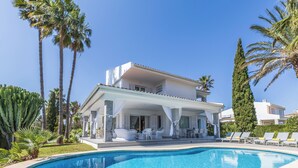 A poolside area with a covered seating area, palm trees, and a clear blue sky. - Can Pedro, elegant villa in Llenaire 3 min walk from the beach! (Port de Pollença)