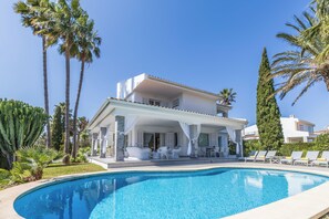 A poolside area with a covered seating area, palm trees, and a clear blue sky. - Can Pedro, elegant villa in Llenaire 3 min walk from the beach! (Port de Pollença)