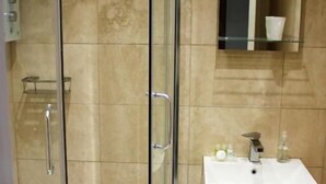 A bathroom with a glass-enclosed shower, a white sink, and a mirror above it. - Pityme Inn (Wadebridge)