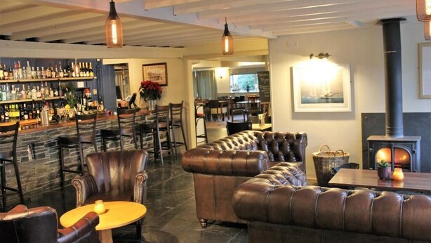 A cozy bar area with leather seating, a fireplace, and a well-stocked bar. - Pityme Inn (Wadebridge)