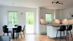Una cocina moderna con armarios blancos, una zona de comedor con sillas negras y un amplio ventanal que proporciona luz natural.