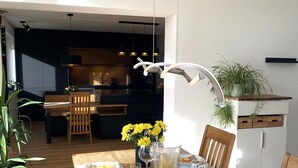 A dining area with a wooden table set for two, a vase with yellow flowers, and a modern pendant light.