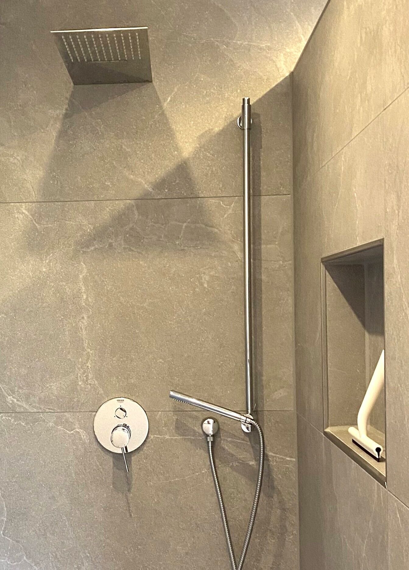 A modern shower with a handheld showerhead and a wall-mounted control panel.