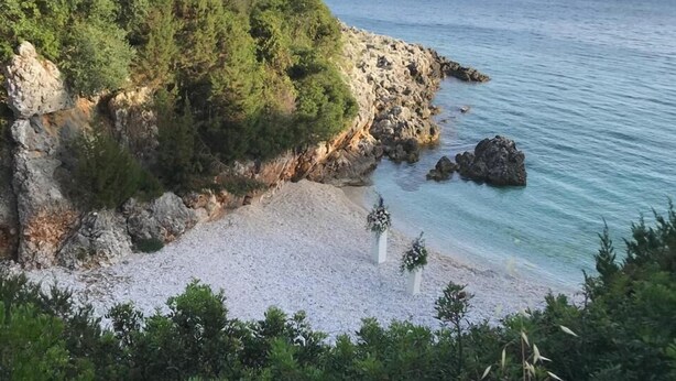A coastal landscape with rocky terrain, a sandy beach, and a clear view of the sea.