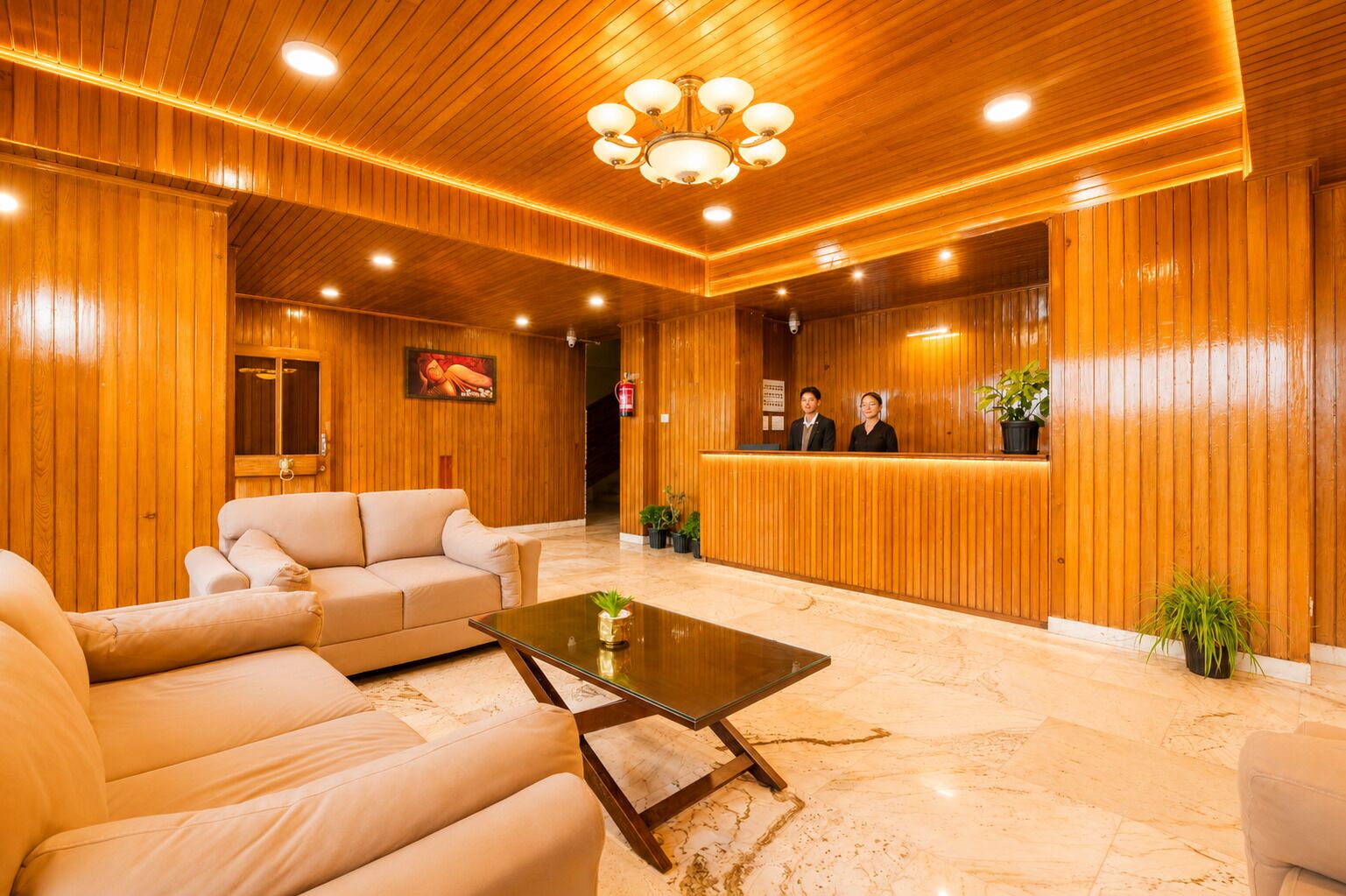 A hotel lobby with wooden paneling, a reception desk, a sofa, a coffee table, and a chandelier.