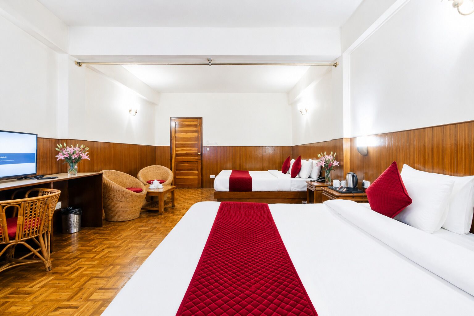 Una habitación de hotel con una cama, dos sillas, un escritorio, un televisor y una puerta de madera.