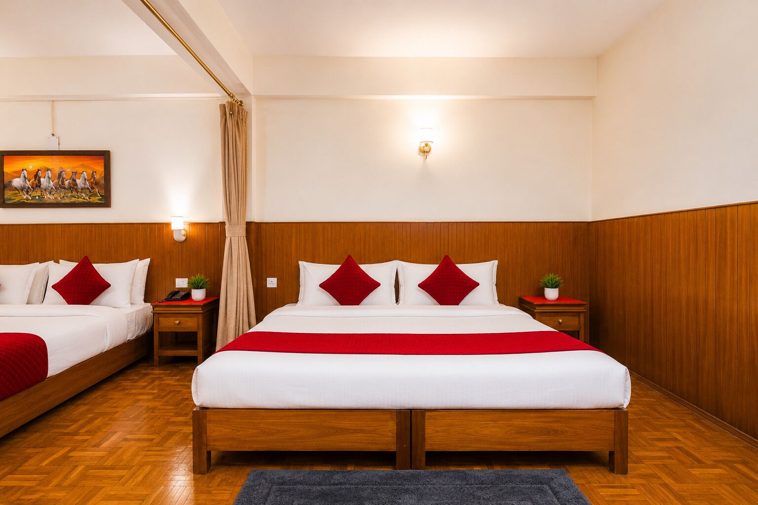 Camera d'albergo con una testata del letto in legno, un letto grande con biancheria da letto bianca e tocchi rossi, un comodino con una lampada, un tavolino con una pianta e un quadro appeso al muro.
