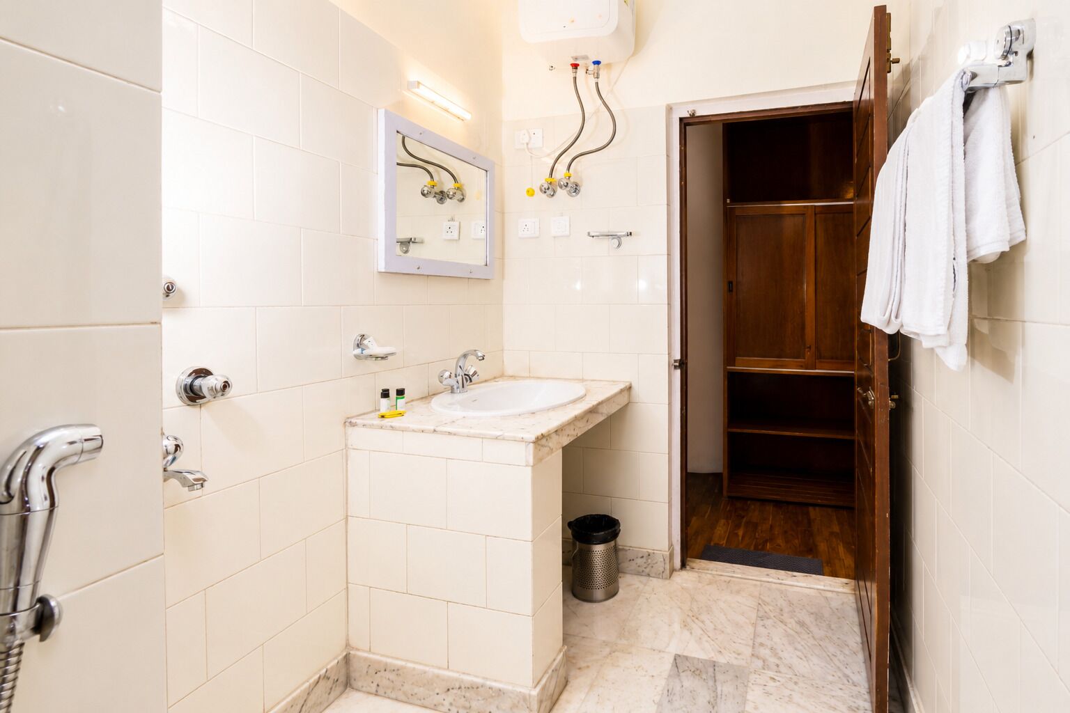 A bathroom with a sink, mirror, towel rack, shower, and a wooden door.