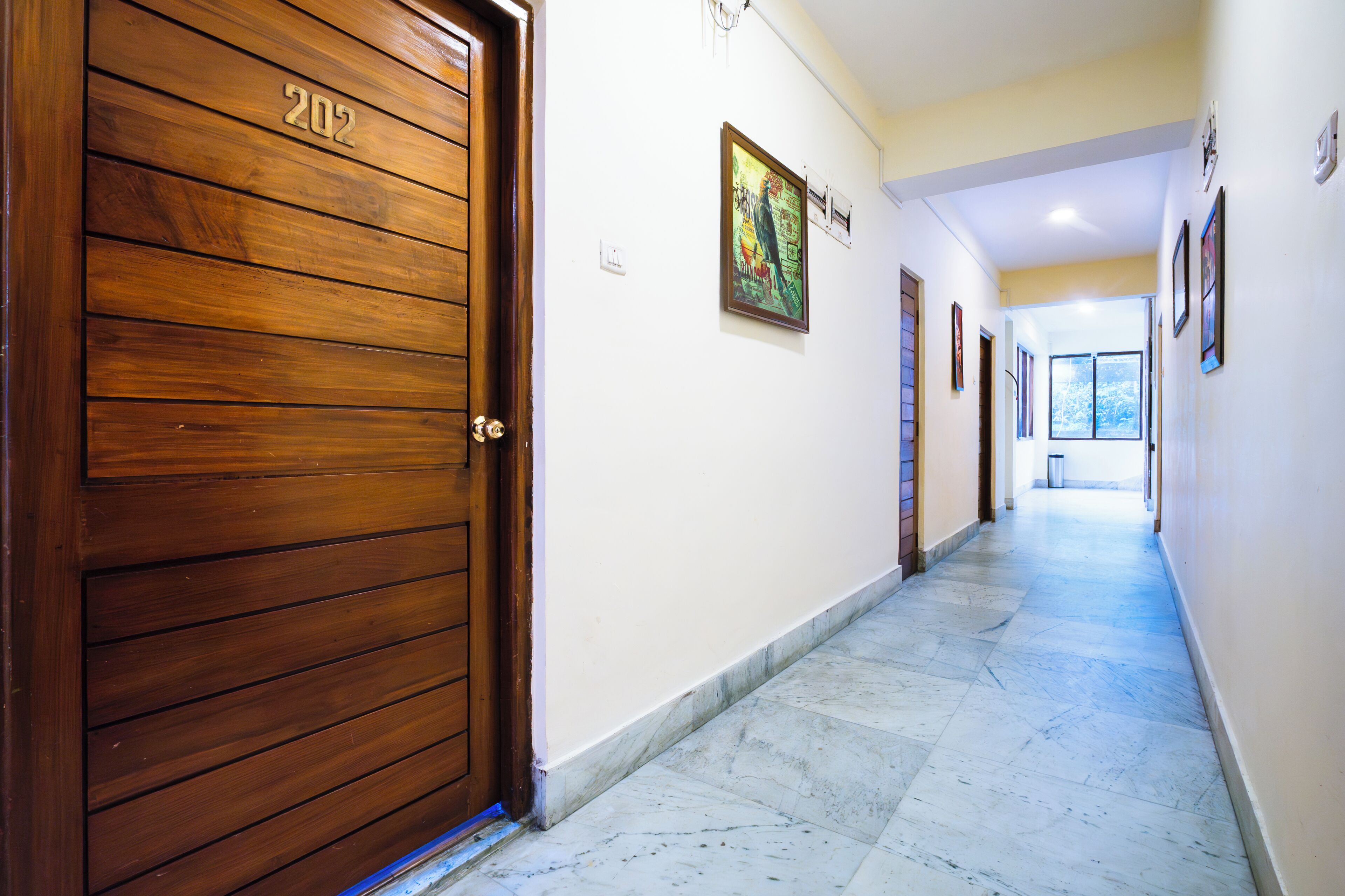 A hallway with a wooden door labeled '202', a tiled floor, and framed artwork on the walls.