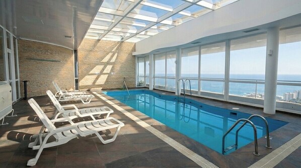 Une piscine intérieure offrant une vue dégagée sur la mer, des chaises longues et un design architectural moderne.