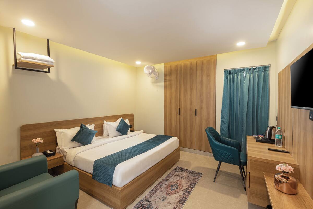 A hotel room with a bed, a desk, a chair, a TV, and a wardrobe.