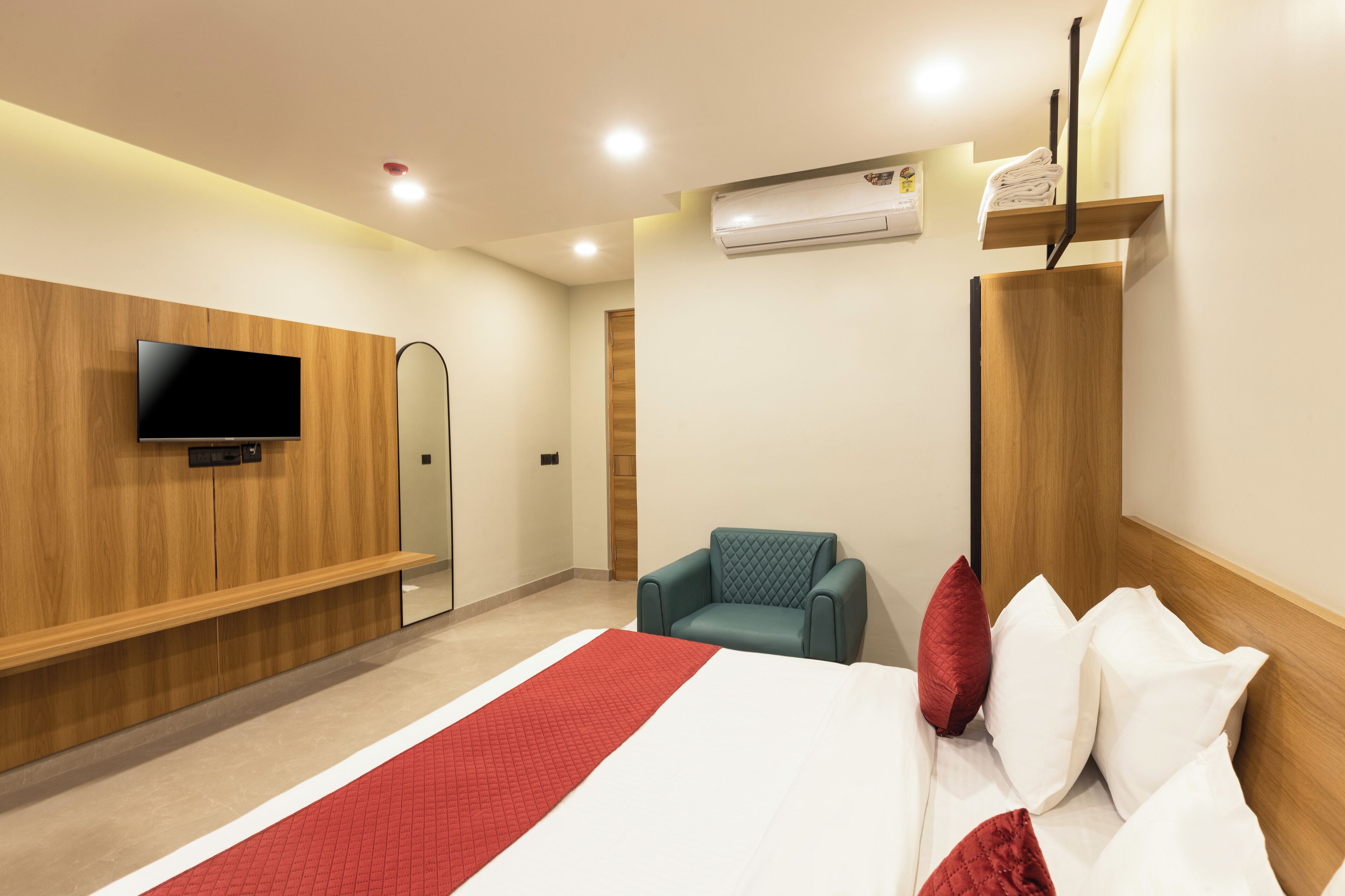 A hotel room with a bed, a TV mounted on the wall, a seating area with a chair, and a wardrobe.