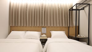 Quarto de hotel com duas camas, cabeceira de madeira, mesa de cabeceira com abajur, secador de cabelo e um aviso na parede.