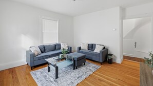 A modern living room with two grey sofas, a glass coffee table, and a wooden floor.
