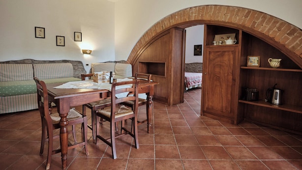 Un coin repas avec une table et des chaises en bois, une arche en briques et, au fond, un canapé vert.