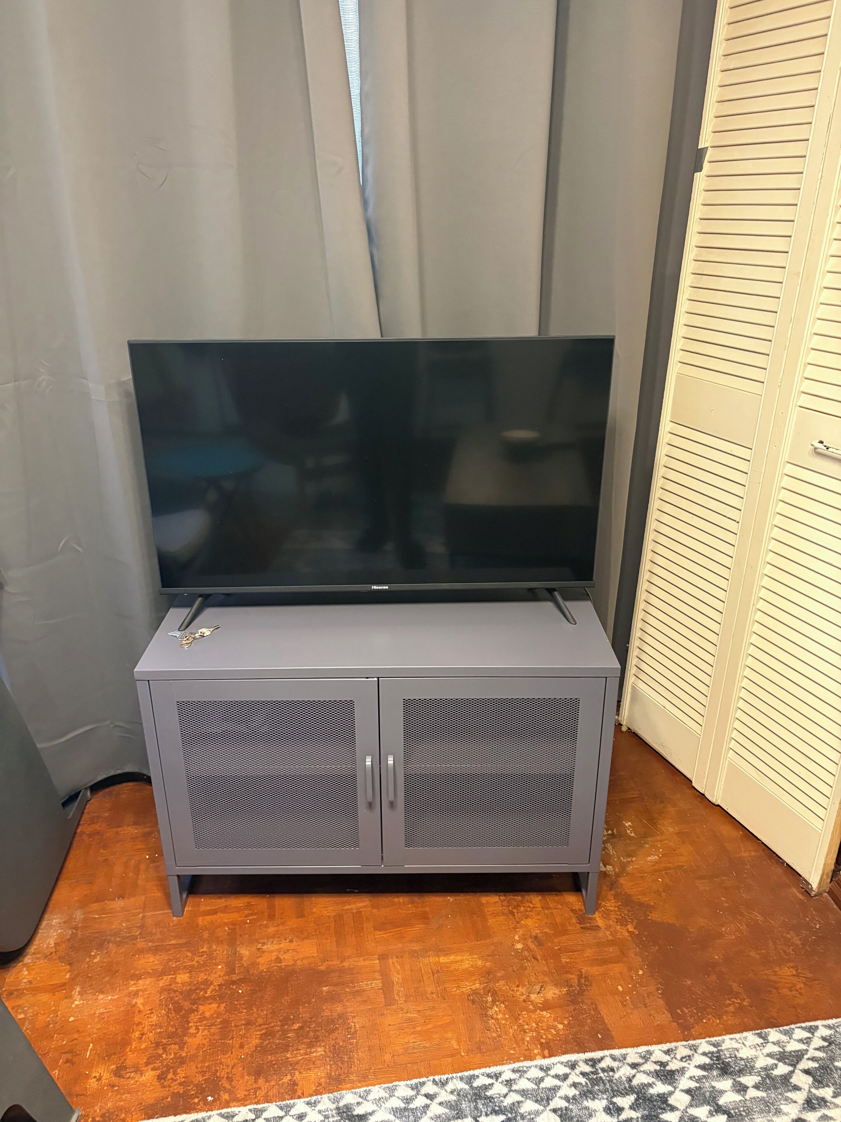 A grey entertainment unit with a flat-screen TV, two cabinets, and a patterned rug.