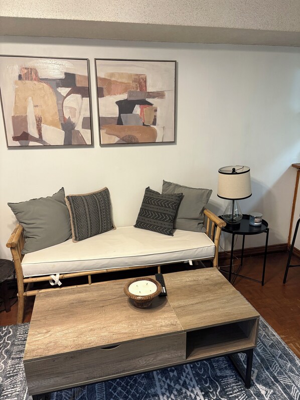 Un salon avec un canapé en bois, deux tableaux abstraits, une table d’appoint avec une lampe et une table basse.