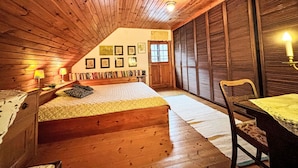 Un dormitorio acogedor en el ático, con techo de madera, una cama, un escritorio y una silla.