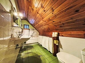 A small, rustic bathroom with a wooden ceiling, green tiled floor, a white sink, and a toilet.
