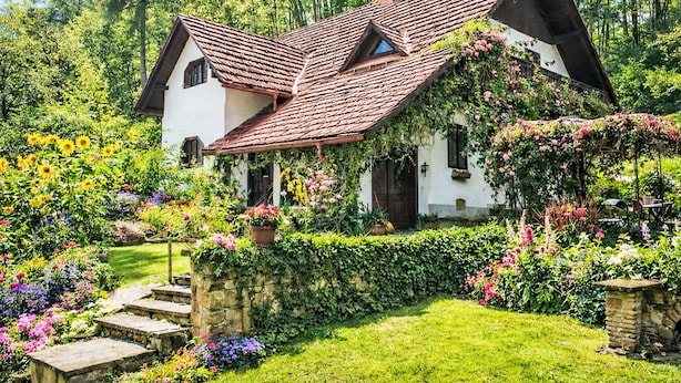 Una casa tradicional con techo inclinado, rodeada de exuberantes jardines y plantas en flor.