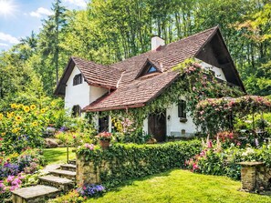 A traditional house with a sloped roof, surrounded by lush gardens and flowering plants.