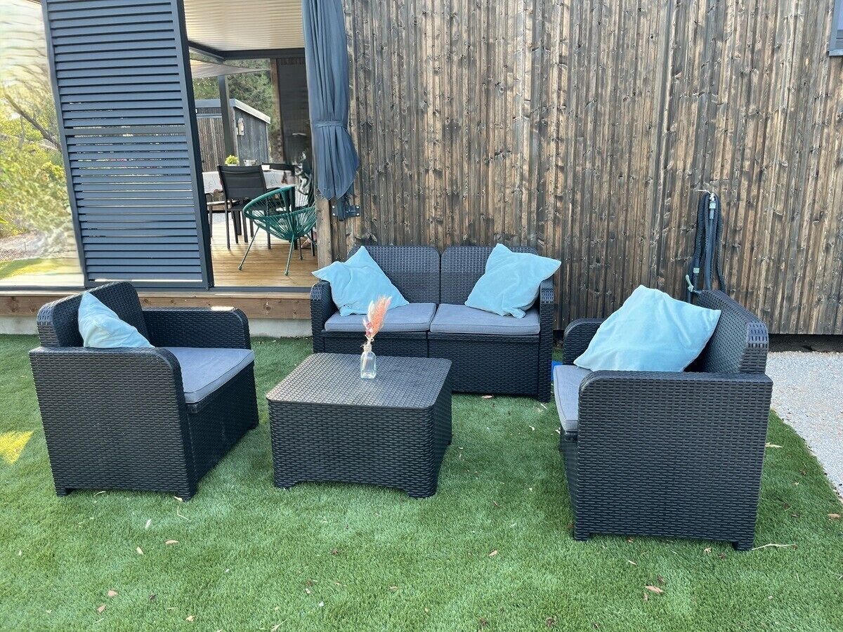 An outdoor seating area with wicker furniture and a small table, set against a wooden fence and a grassy lawn.