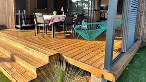 A wooden deck with a table and chairs, a hanging chair, and a glass door leading inside. - Chalet Prestige le Paradis - villa Cap d' Agde (Agde)