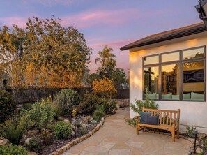 A garden pathway leading to a house with a bench and a window overlooking the garden.