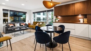 Un soggiorno moderno con divano, tavolino, poltrone, un tavolo da pranzo rotondo e un'area cucina con pensili in legno e un lampadario.