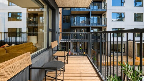 Un balcone con pavimento in legno, mobili in vimini e vista sui palazzi vicini.