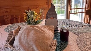 Ett mysigt rum med en väggpanel av trä, en korg av rotting, en välkomstskylt, en vas med blommor och ett bord med ett mönstrat bordsduk.