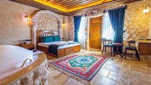 A room with a large bed, a wooden desk, a stone wall, and a bathtub. - Bloom Cappadocia Hotel (Nevsehir)