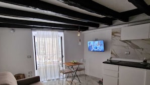 Ein modernes Wohnzimmer mit einer Couch, einem Essbereich mit Tisch und Stühlen, einer Küche und einem Fernseher sowie einem großen Fenster mit Vorhängen.