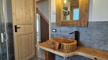 Una porta in legno, un mobile bagno in legno con lavabo, uno specchio e un lampadario.