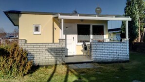 Una casa de un piso con un porche delantero, una antena parabólica y un ventanal pequeño.