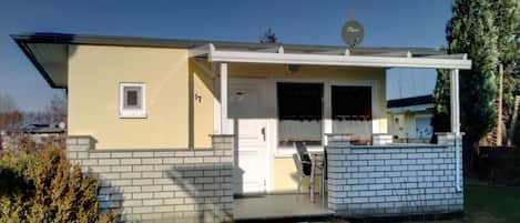 Uma casa térrea com varanda frontal, antena parabólica e uma janela pequena.