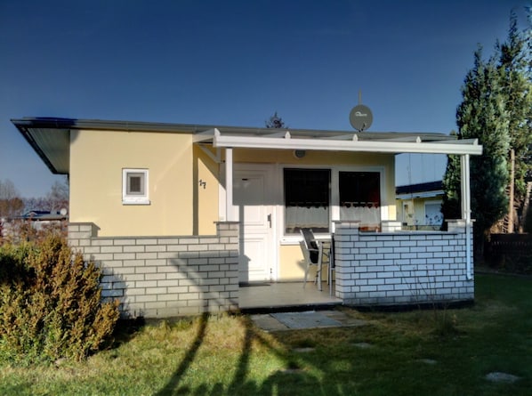 A single-story house with a front porch, a satellite dish, and a small window. - Dünenbungalow I - Vacation bungalow for 4 people, 700 meters from the beach in Graal-Müritz (Graal-Müritz)
