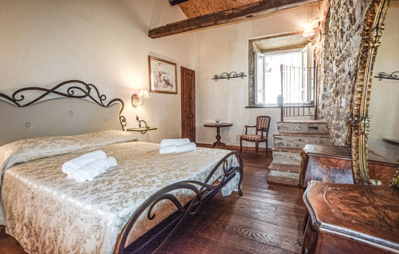 A bedroom with a bed, a chair, a small table, and a staircase leading to an upper level.