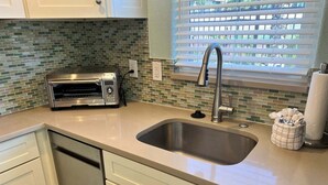 Una cocina con un lavaplatos de acero inoxidable, un horno tostador y una ventana con persianas.