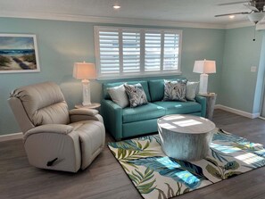 Ein Wohnzimmer mit einem petrolfarbenen Sofa, einem beigen Sessel, einem runden Couchtisch und einem gemusterten Teppich.