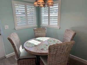A dining area with a round table, four wicker chairs, and a ceiling light fixture. - Casa Blanca - Villa D08 (Siesta Key)