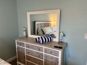A bedroom with a dresser, a mirror, a lamp, and a bed with pillows. - Casa Blanca - Villa D08 (Siesta Key)