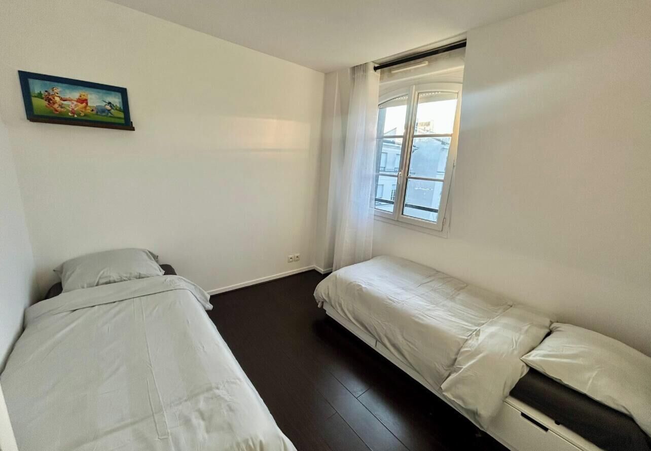 Un apartamento pequeño de una habitación con dos camas, una ventana con cortinas e imagen colgada en la pared.