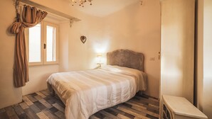 Una camera da letto con un letto, un comodino, una cassettiera, una finestra con tende e un termosifone a parete.