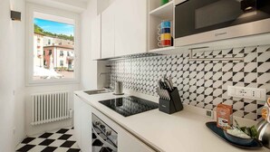 A modern kitchen with a black and white checkered floor, a window with a view of buildings, and a microwave above the counter. - Welcome to Pietra Futura, your ideal refuge in the heart of Pignone. Located in the picturesque town square, this newly renovated home offers an authentic experience of Liguria and its fascinating hinterland. Just 20 minutes drive from the famous Cinque  (Pignone)