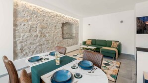 A dining area with a stone wall, a green sofa, and a TV in the background. - Welcome to Pietra Futura, your ideal refuge in the heart of Pignone. Located in the picturesque town square, this newly renovated home offers an authentic experience of Liguria and its fascinating hinterland. Just 20 minutes drive from the famous Cinque  (Pignone)