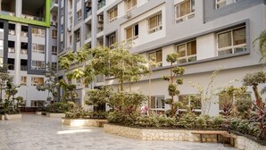 Un immeuble à plusieurs étages doté d’une cour intérieure agrémentée de jardinières en pierre et de différents arbres.