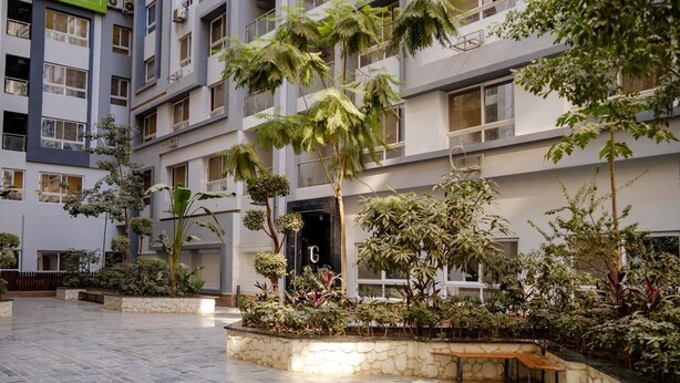Un immeuble à plusieurs étages doté d’une cour intérieure agrémentée de jardinières en pierre, de bancs et de diverses plantes.