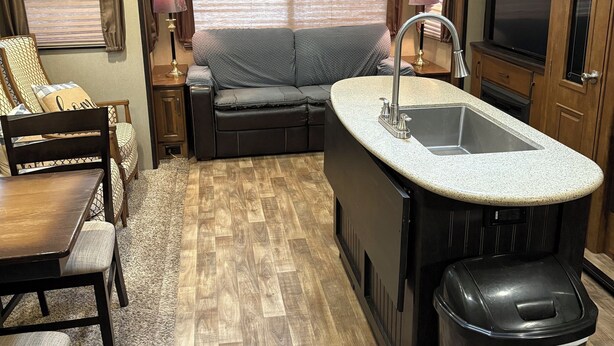 A compact RV kitchen with a central island, a sink, and a trash can. - Cozy 1-bedroom caravan in lovely Aiken with AC (Aiken)