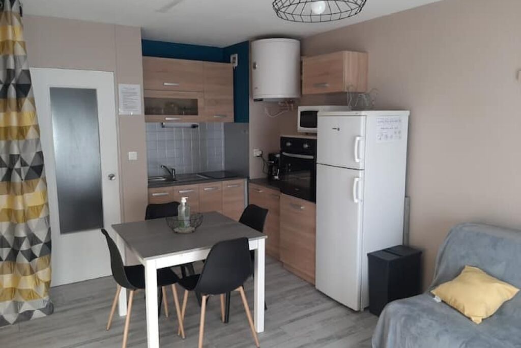 A compact kitchen with a microwave, oven, and refrigerator. There is a dining table with chairs and a sofa in the living area.